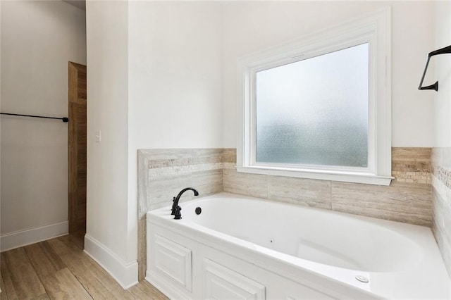 bathroom with a bath, baseboards, and wood finished floors