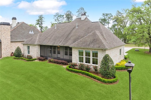 rear view of property featuring brick siding, roof with shingles, a chimney, and a lawn