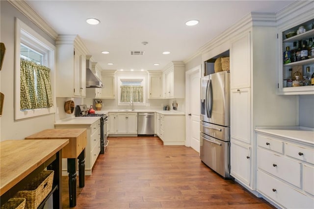 kitchen with stainless steel appliances, wall chimney exhaust hood, a sink, dark wood-style flooring, and light countertops