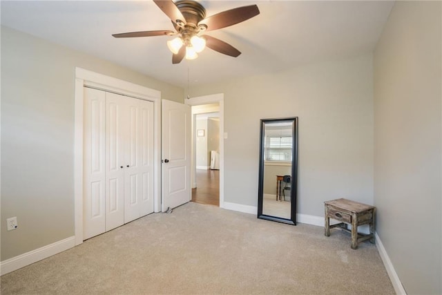unfurnished bedroom with light carpet, a closet, baseboards, and a ceiling fan