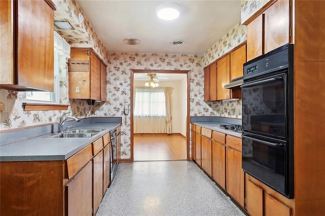 1017 Elmeer Ave, Metairie, LA 70005 - kitchen featuring wallpapered walls, a sink, under cabinet range hood, ceiling fan, and brown cabinetry