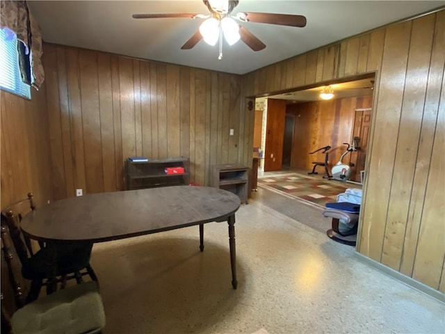 home office with a ceiling fan and wood walls