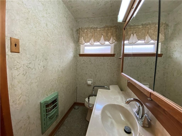 bathroom with toilet, heating unit, a healthy amount of sunlight, and a sink