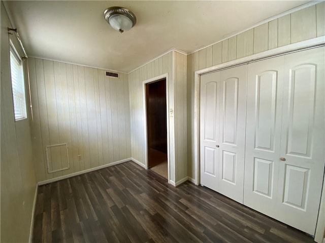 unfurnished bedroom featuring visible vents, a closet, baseboards, dark wood-style flooring, and wooden walls