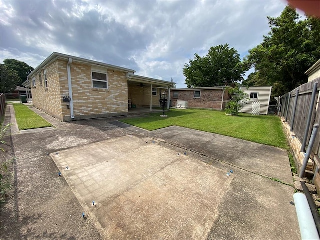 back of property with a patio, a lawn, a ceiling fan, brick siding, and a fenced backyard