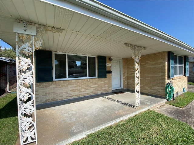 view of exterior entry featuring a porch and brick siding