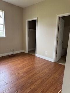unfurnished bedroom featuring wood finished floors, baseboards, a closet, and ensuite bath