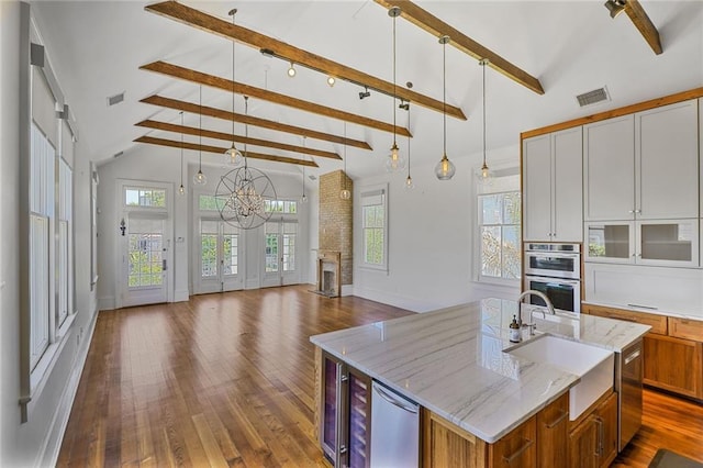 kitchen featuring a center island with sink, brown cabinets, beam ceiling, dark wood finished floors, and double oven