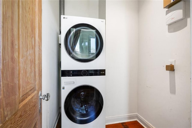 clothes washing area with baseboards, stacked washer / drying machine, laundry area, and wood finished floors
