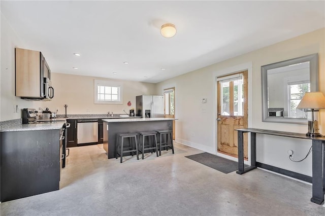 kitchen featuring a kitchen breakfast bar, baseboards, a kitchen island, appliances with stainless steel finishes, and finished concrete floors
