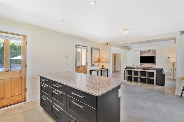 kitchen featuring visible vents, baseboards, dark cabinetry, a kitchen island, and light stone counters