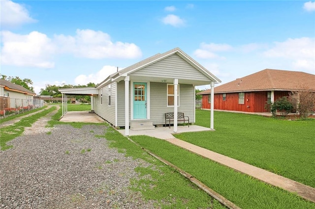 shotgun-style home featuring entry steps, fence, a front lawn, an attached carport, and driveway