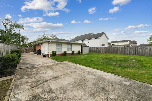 5387 Chamberlain Dr, New Orleans, LA 70122 - rear view of house featuring a yard, a fenced backyard, an outdoor structure, a storage unit, and concrete driveway