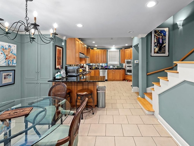 kitchen with a peninsula, a chandelier, under cabinet range hood, stainless steel appliances, and baseboards