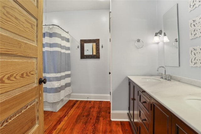 bathroom featuring baseboards, double vanity, a shower with curtain, a sink, and wood finished floors