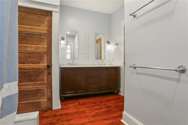 full bath featuring baseboards, a sink, double vanity, and wood finished floors