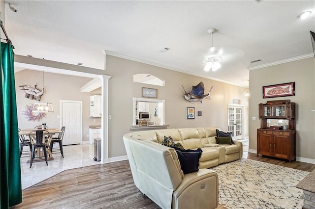 living area featuring visible vents, wood finished floors, baseboards, ceiling fan with notable chandelier, and ornamental molding