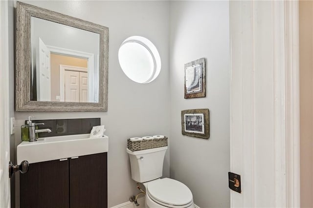 half bath featuring baseboards, vanity, and toilet