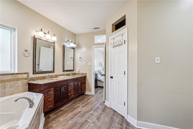 full bathroom featuring a sink, double vanity, wood finished floors, visible vents, and a bath