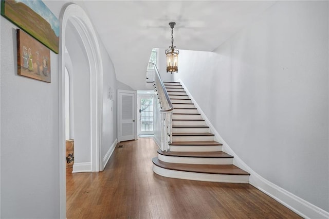 58 Fontainebleau Dr, New Orleans, LA 70125 - staircase with baseboards, arched walkways, wood finished floors, and a notable chandelier