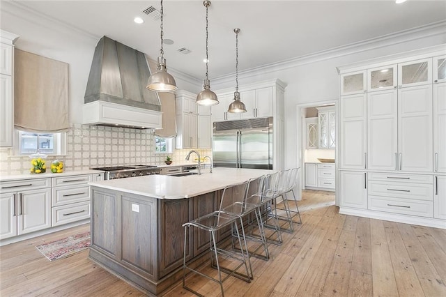 316 Sena Dr, Metairie, LA 70005 - kitchen with custom exhaust hood, a kitchen island with sink, light countertops, a kitchen bar, and appliances with stainless steel finishes
