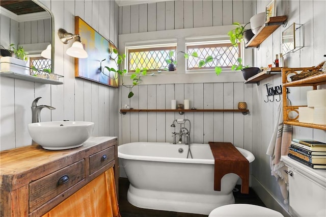bathroom featuring wood walls, toilet, a freestanding bath, and vanity