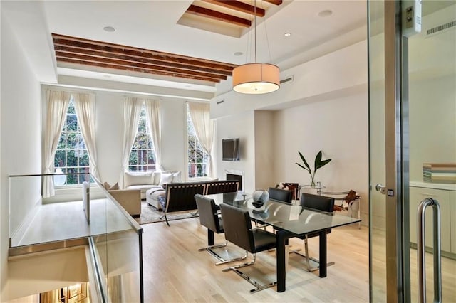 dining area featuring beamed ceiling, light wood-type flooring, and a tray ceiling