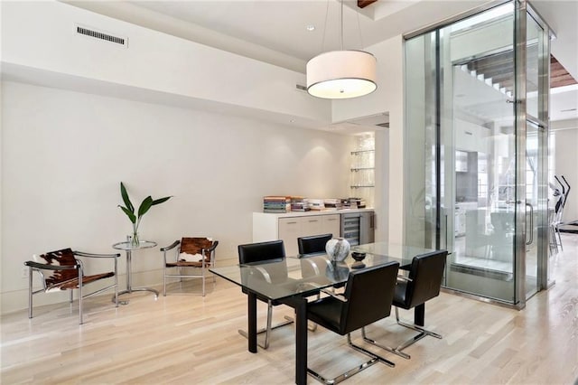 dining room featuring light wood finished floors, wine cooler, visible vents, and a high ceiling