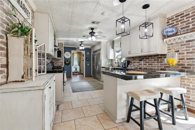 313 Sarah Victoria Dr, Belle Chasse, LA 70037 - kitchen with brick wall, a peninsula, dark countertops, visible vents, and ceiling fan