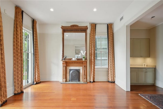 unfurnished living room with wood finished floors, baseboards, a fireplace with raised hearth, a sink, and recessed lighting