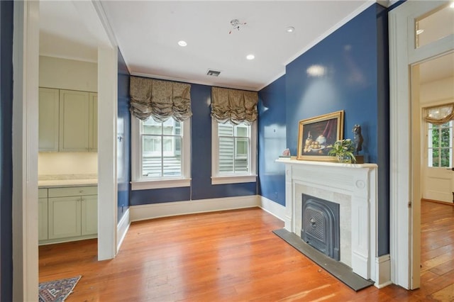 unfurnished living room with ornamental molding, light wood-style flooring, baseboards, a high end fireplace, and recessed lighting