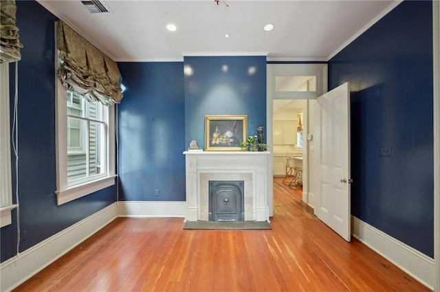 unfurnished living room featuring wood finished floors, a fireplace with raised hearth, ornamental molding, baseboards, and recessed lighting