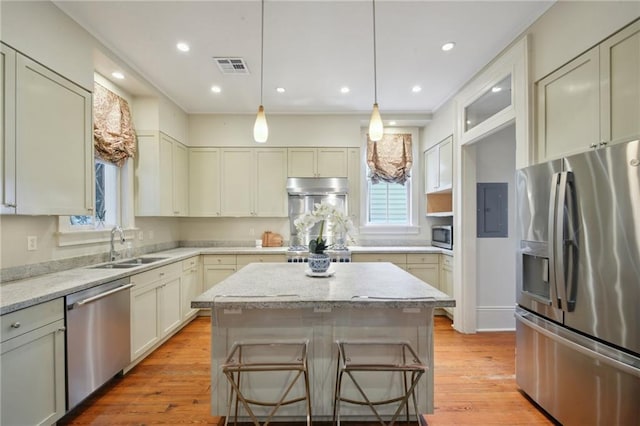 kitchen with stainless steel appliances, a sink, a kitchen island, light stone counters, and light wood-style flooring