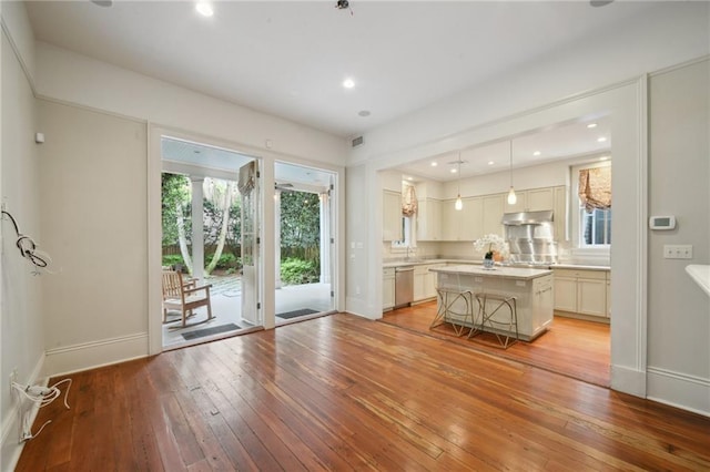 kitchen with under cabinet range hood, light wood-type flooring, a center island, light countertops, and baseboards