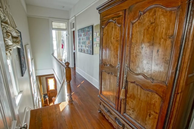 hallway featuring an upstairs landing, dark wood-type flooring, baseboards, and healthy amount of natural light