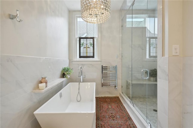 full bath featuring tile walls, a shower stall, a chandelier, a soaking tub, and a towel warming rack