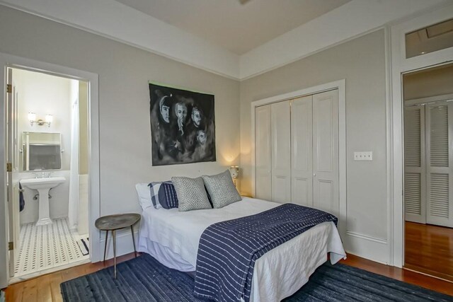 bedroom with wood finished floors, a closet, connected bathroom, and a sink