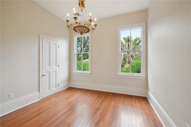 empty room with a chandelier, plenty of natural light, light wood finished floors, and baseboards