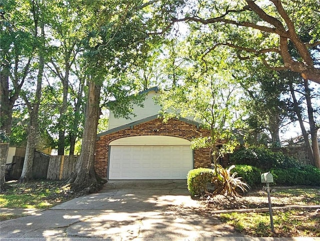 view of front facade featuring an attached garage, driveway, fence, and brick siding