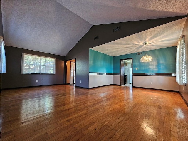 unfurnished living room with wood-type flooring, visible vents, a textured ceiling, and an inviting chandelier