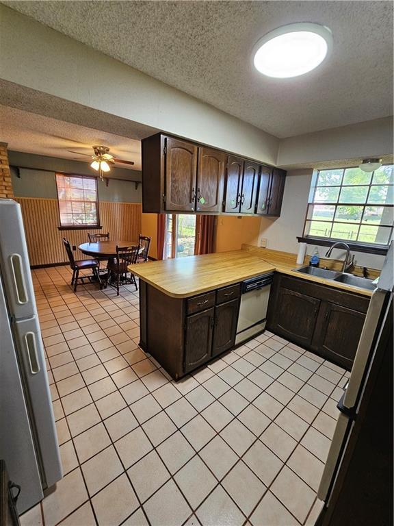 kitchen with a textured ceiling, dark brown cabinets, stainless steel refrigerator with ice dispenser, dishwasher, and a sink