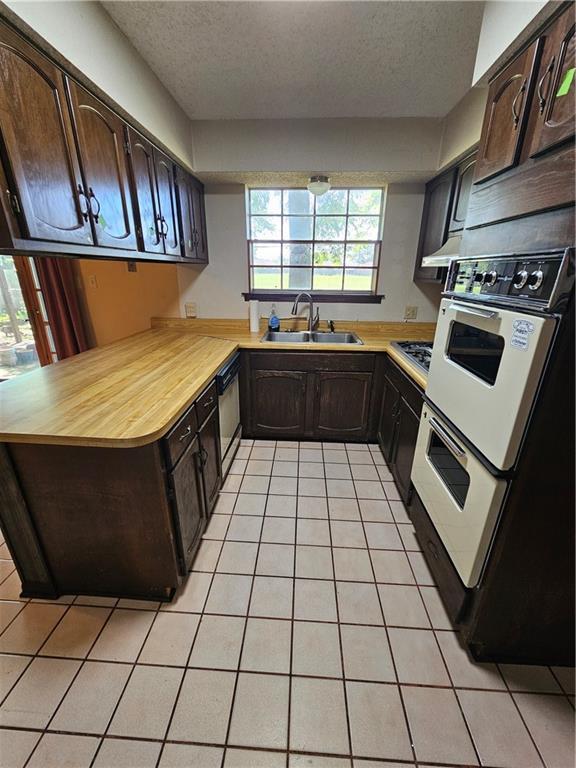 kitchen featuring a textured ceiling, light tile patterned flooring, a sink, and dark brown cabinets