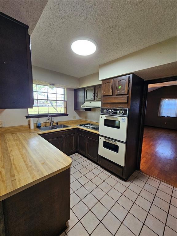 kitchen with under cabinet range hood, light tile patterned floors, a sink, and dark brown cabinets