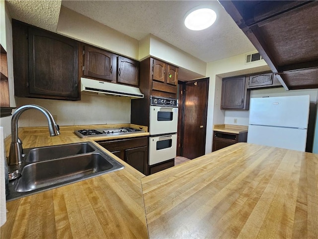 kitchen with range hood, white appliances, dark brown cabinetry, visible vents, and a sink