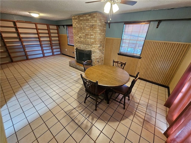 dining room with light tile patterned flooring, a textured ceiling, ceiling fan, and a brick fireplace