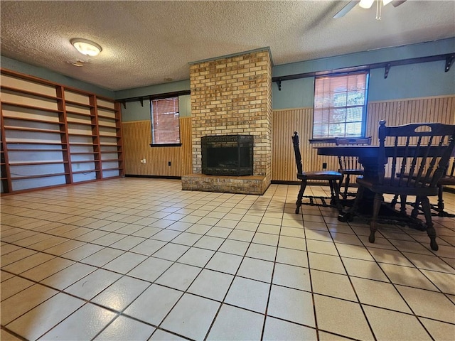 dining area with ceiling fan, a fireplace, a textured ceiling, a wainscoted wall, and wooden walls