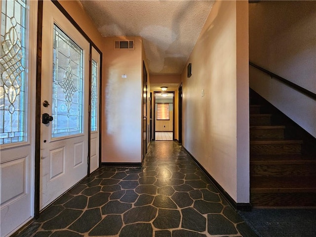entrance foyer featuring a textured ceiling, baseboards, visible vents, and stairs