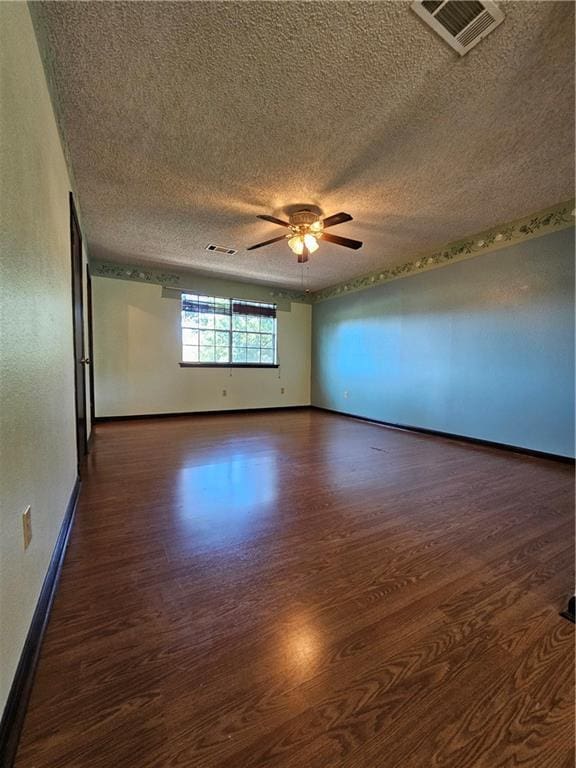 spare room with baseboards, a textured ceiling, dark wood-type flooring, visible vents, and ceiling fan