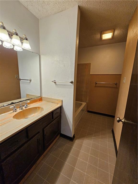 full bath featuring tile patterned flooring, vanity, and a textured ceiling