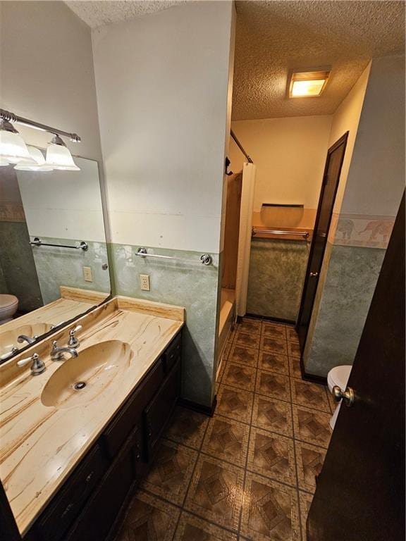 bathroom featuring a shower with shower curtain, toilet, a textured ceiling, vanity, and a wainscoted wall